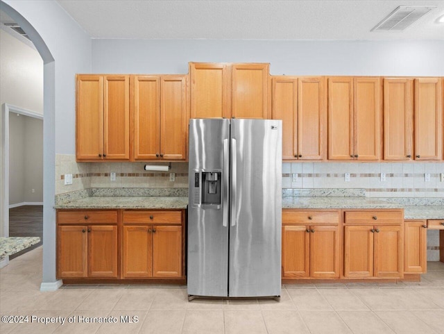 kitchen featuring backsplash, light stone countertops, stainless steel refrigerator with ice dispenser, and light tile patterned floors