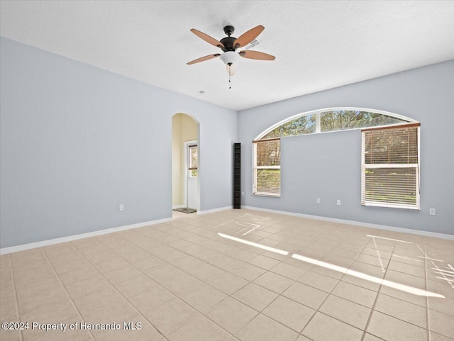 empty room with a textured ceiling, ceiling fan, and light tile patterned flooring