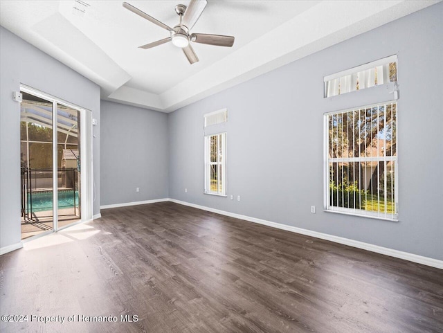 empty room with dark hardwood / wood-style floors, ceiling fan, and a raised ceiling