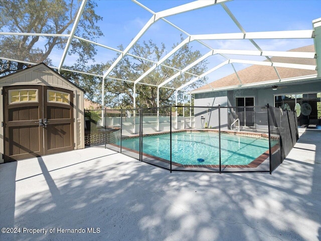 view of swimming pool featuring a lanai, ceiling fan, a patio, and a shed