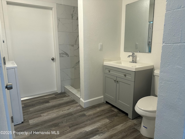 bathroom with washer / dryer, wood-type flooring, vanity, toilet, and a tile shower