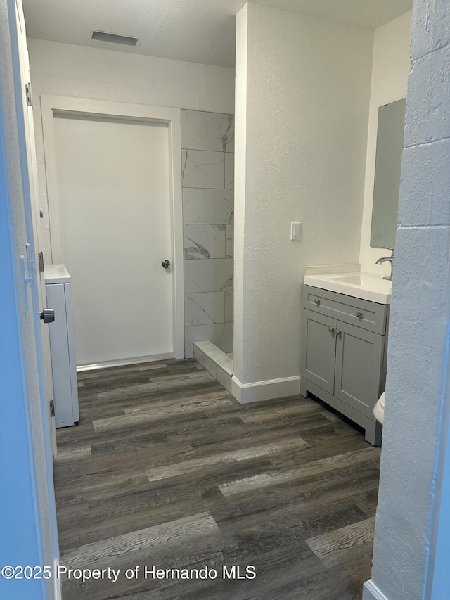 bathroom with washer / dryer, a tile shower, wood-type flooring, and vanity