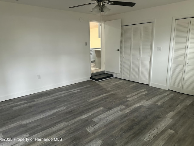 unfurnished bedroom with ceiling fan, two closets, and dark hardwood / wood-style floors