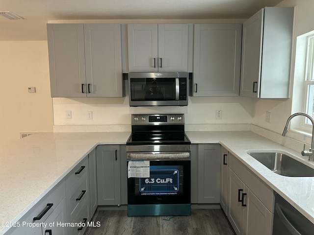 kitchen with light stone countertops, gray cabinets, appliances with stainless steel finishes, and sink