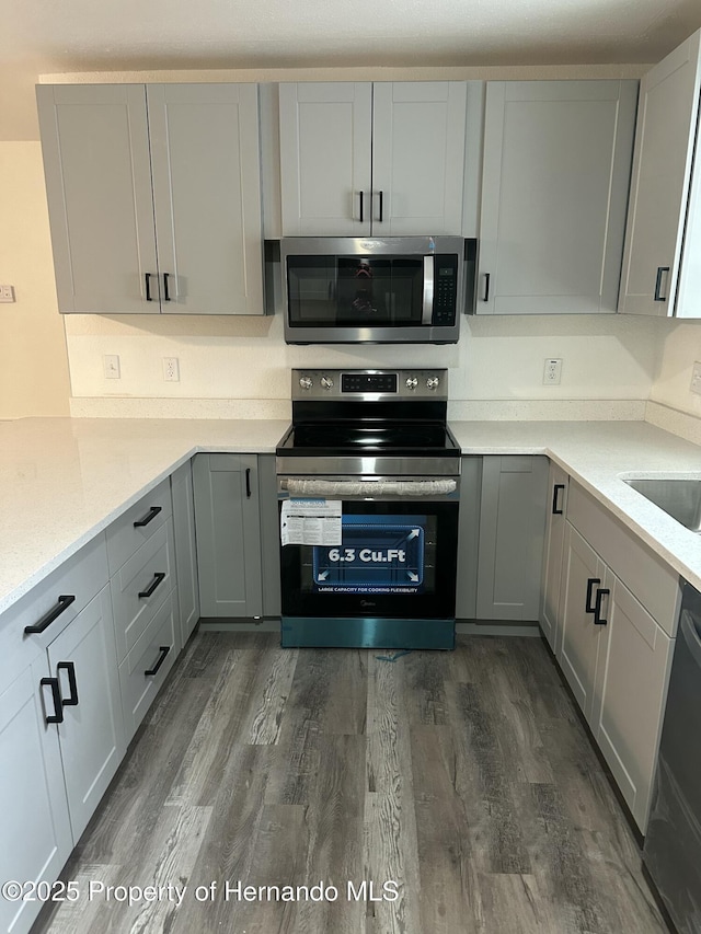 kitchen featuring dark hardwood / wood-style floors, gray cabinets, sink, light stone countertops, and stainless steel appliances