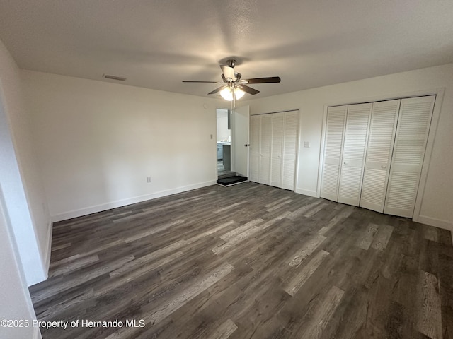 unfurnished bedroom featuring ceiling fan, dark hardwood / wood-style floors, and multiple closets