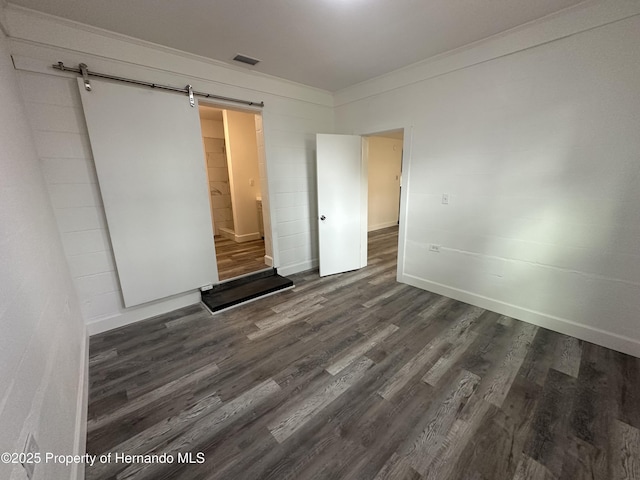 interior space with dark hardwood / wood-style floors, ornamental molding, and a barn door