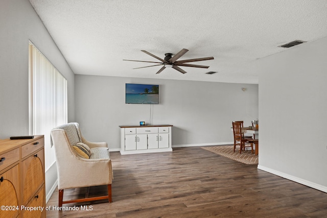 living area with ceiling fan, dark wood-type flooring, and a textured ceiling