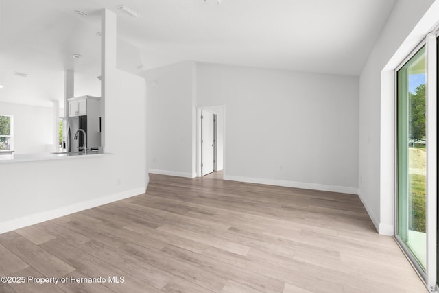 unfurnished living room featuring light wood-style floors, lofted ceiling, and baseboards