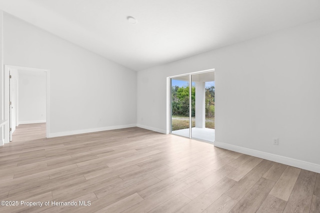 empty room with light wood-style floors, lofted ceiling, and baseboards