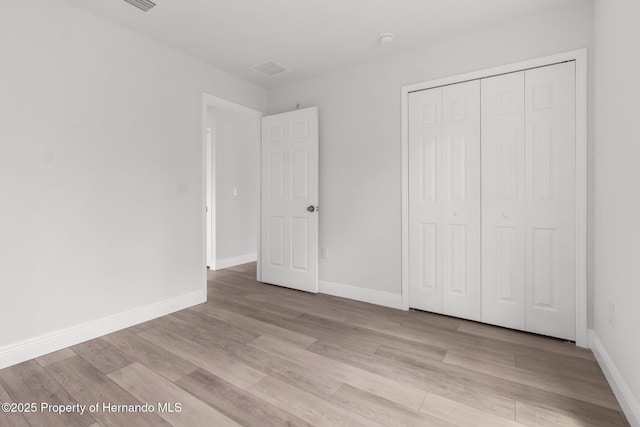 unfurnished bedroom with a closet, baseboards, and light wood finished floors