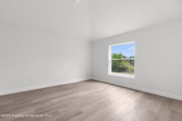 empty room featuring vaulted ceiling, light wood-type flooring, and baseboards