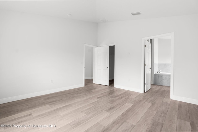 unfurnished bedroom with visible vents, baseboards, lofted ceiling, ensuite bath, and light wood-style flooring