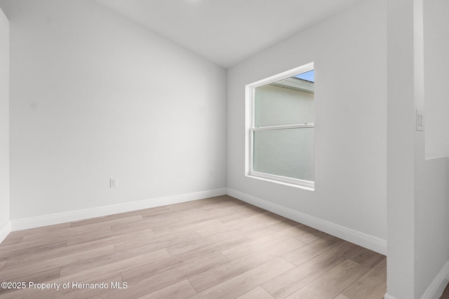 spare room featuring lofted ceiling, baseboards, and light wood finished floors