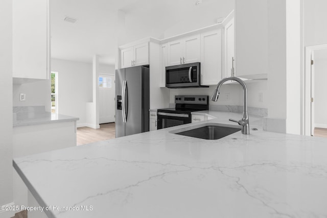 kitchen with light stone counters, appliances with stainless steel finishes, light wood-style floors, white cabinets, and a sink