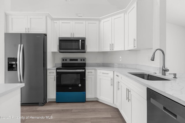 kitchen featuring appliances with stainless steel finishes, light stone counters, light wood-style floors, white cabinetry, and a sink