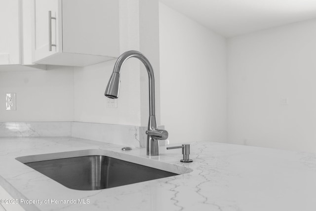 details with light stone counters, white cabinetry, and a sink