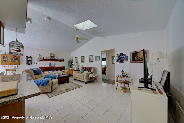 living room featuring ceiling fan, light tile patterned flooring, lofted ceiling with skylight, and a textured ceiling