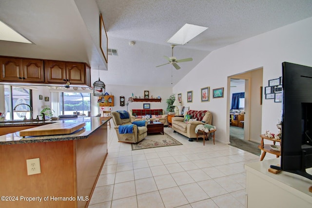 tiled living room with lofted ceiling with skylight, sink, ceiling fan, and a textured ceiling