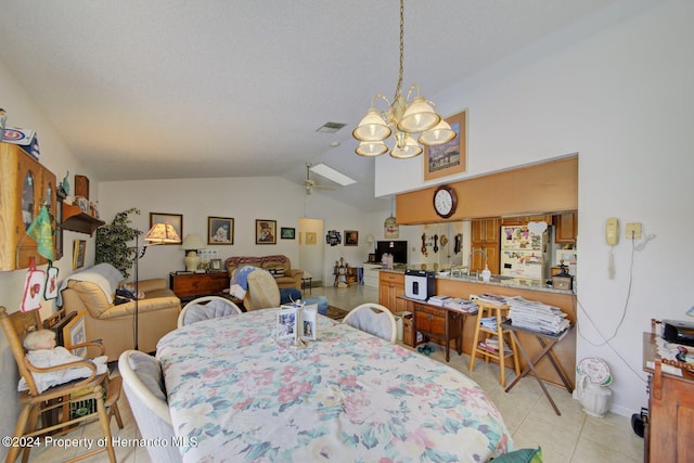 dining room with ceiling fan with notable chandelier, light tile patterned floors, and vaulted ceiling