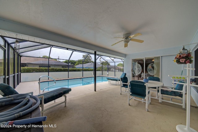 view of swimming pool featuring glass enclosure, ceiling fan, and a patio area