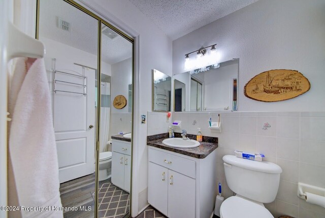 bathroom with vanity, toilet, a textured ceiling, tile walls, and wood-type flooring