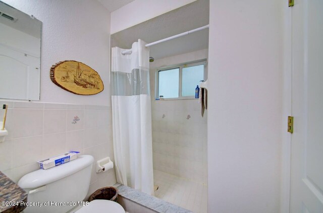 bathroom with a shower with curtain, toilet, and tile walls