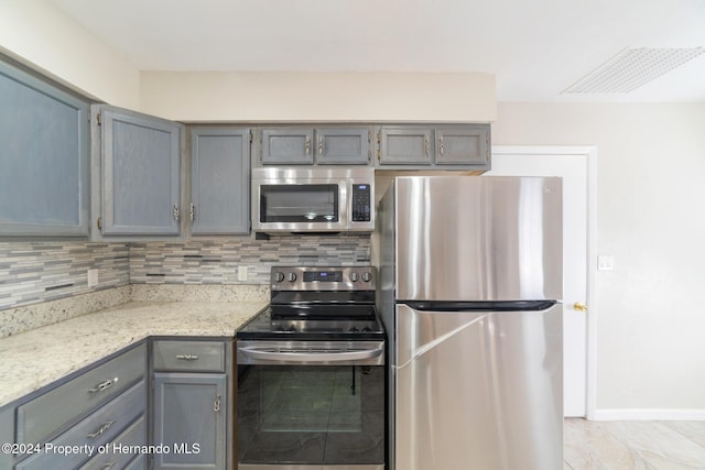 kitchen featuring gray cabinets, light stone countertops, stainless steel appliances, and tasteful backsplash