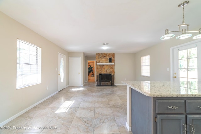 kitchen with decorative light fixtures, a stone fireplace, and light stone counters