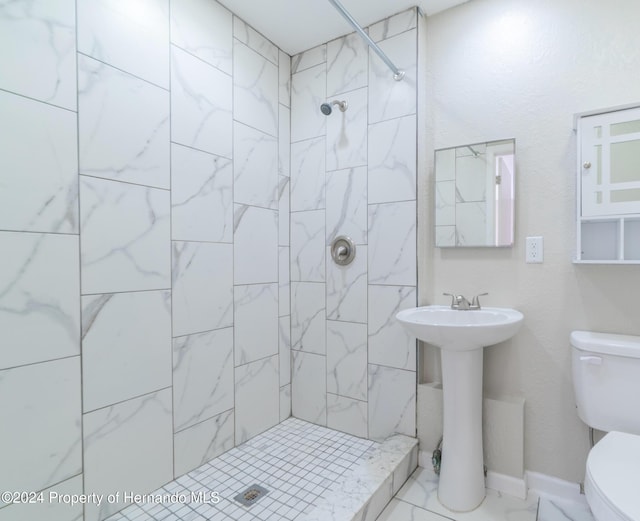 bathroom featuring toilet, a tile shower, and sink