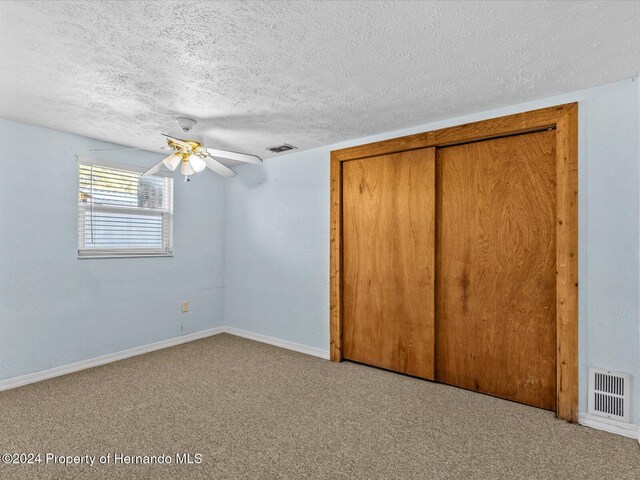 unfurnished bedroom with carpet flooring, ceiling fan, a textured ceiling, and a closet