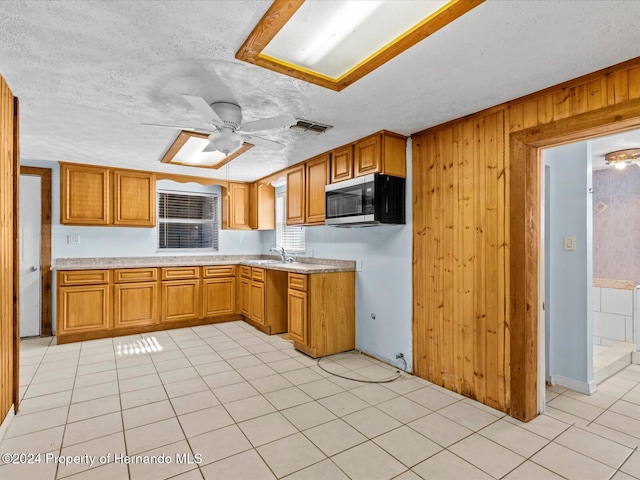 kitchen featuring sink, wooden walls, ceiling fan, light tile patterned floors, and a textured ceiling