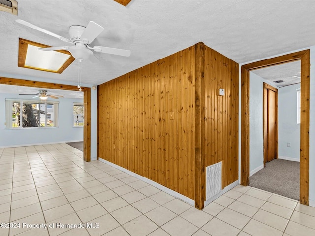 tiled empty room with a textured ceiling, a skylight, ceiling fan, and wooden walls