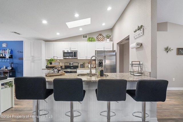 kitchen with white cabinetry, sink, lofted ceiling with skylight, light hardwood / wood-style floors, and appliances with stainless steel finishes