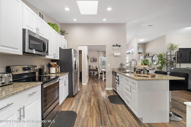 kitchen with dark wood-type flooring, white cabinets, sink, a skylight, and stainless steel appliances