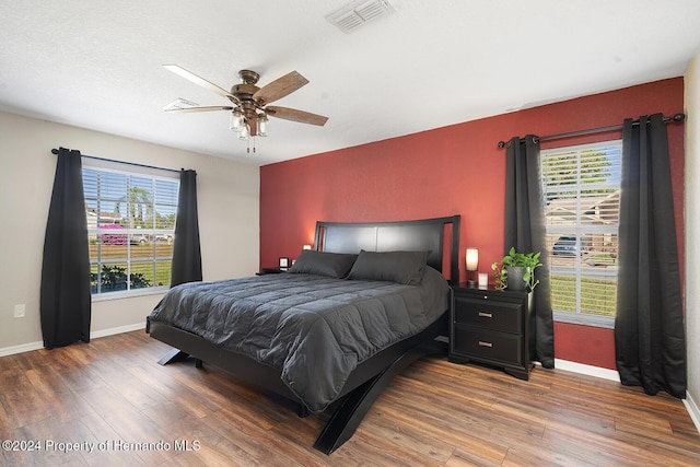 bedroom featuring ceiling fan, dark hardwood / wood-style floors, and multiple windows