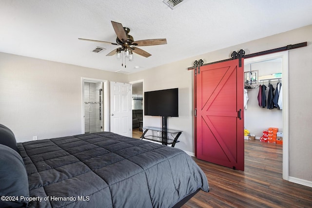 bedroom featuring a textured ceiling, ceiling fan, dark wood-type flooring, a barn door, and a closet