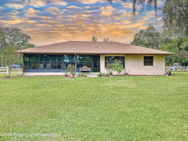 back house at dusk featuring a yard and a sunroom