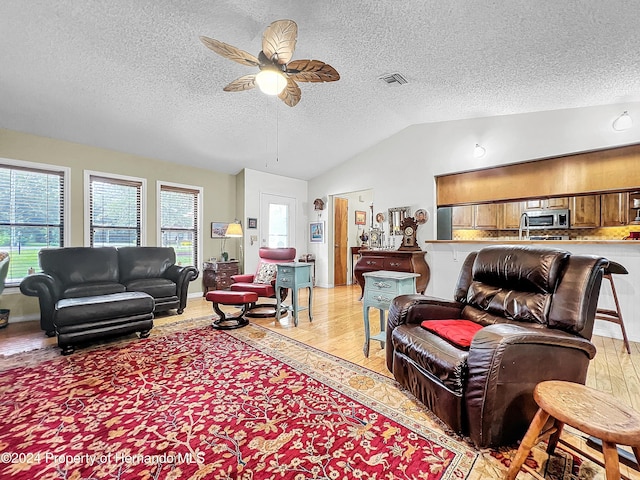 living room featuring a textured ceiling, ceiling fan, light hardwood / wood-style floors, and vaulted ceiling