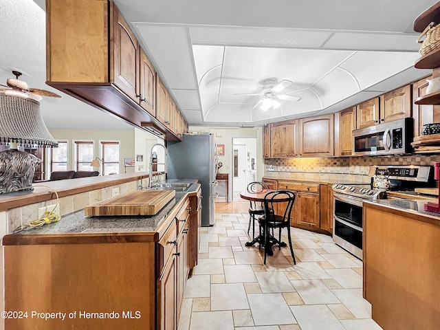 kitchen with ceiling fan, sink, a tray ceiling, decorative backsplash, and appliances with stainless steel finishes