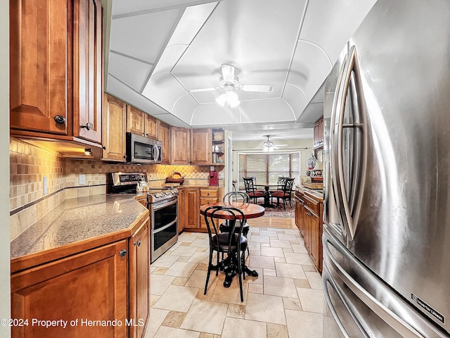 kitchen featuring ceiling fan, stainless steel appliances, a tray ceiling, and tasteful backsplash