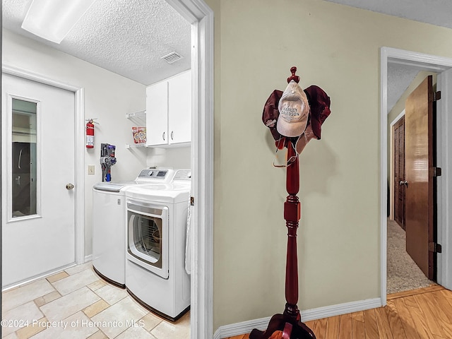 laundry room featuring independent washer and dryer, cabinets, a textured ceiling, and light wood-type flooring