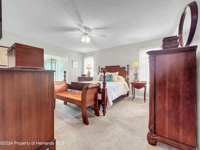 bedroom with a textured ceiling, light colored carpet, multiple windows, and ceiling fan