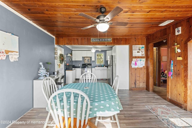 dining room featuring wood ceiling, ceiling fan, crown molding, wooden walls, and hardwood / wood-style flooring