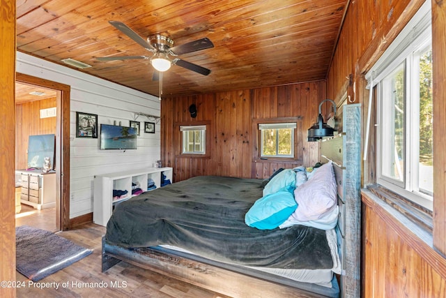 bedroom with wood walls, wood-type flooring, and multiple windows