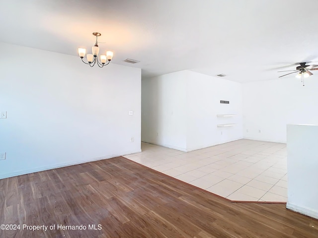 empty room featuring ceiling fan with notable chandelier and light wood-type flooring