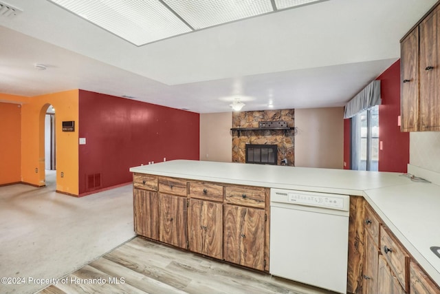 kitchen featuring dishwasher, light hardwood / wood-style flooring, a fireplace, and kitchen peninsula