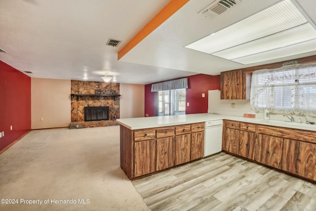 kitchen with sink, white dishwasher, a fireplace, light hardwood / wood-style floors, and kitchen peninsula