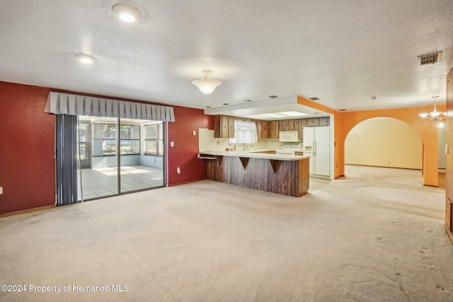 kitchen with light carpet, white appliances, kitchen peninsula, and a textured ceiling