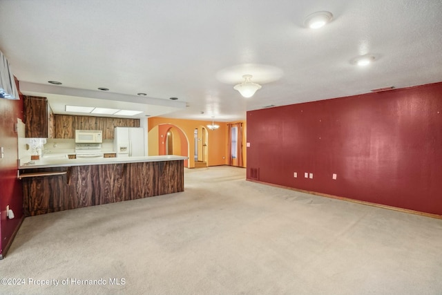 kitchen featuring white appliances, kitchen peninsula, light carpet, and a notable chandelier